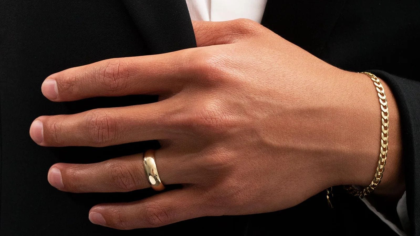 close-up of a man in a black suit and white shirt wearing a gold wedding band and gold bracelet