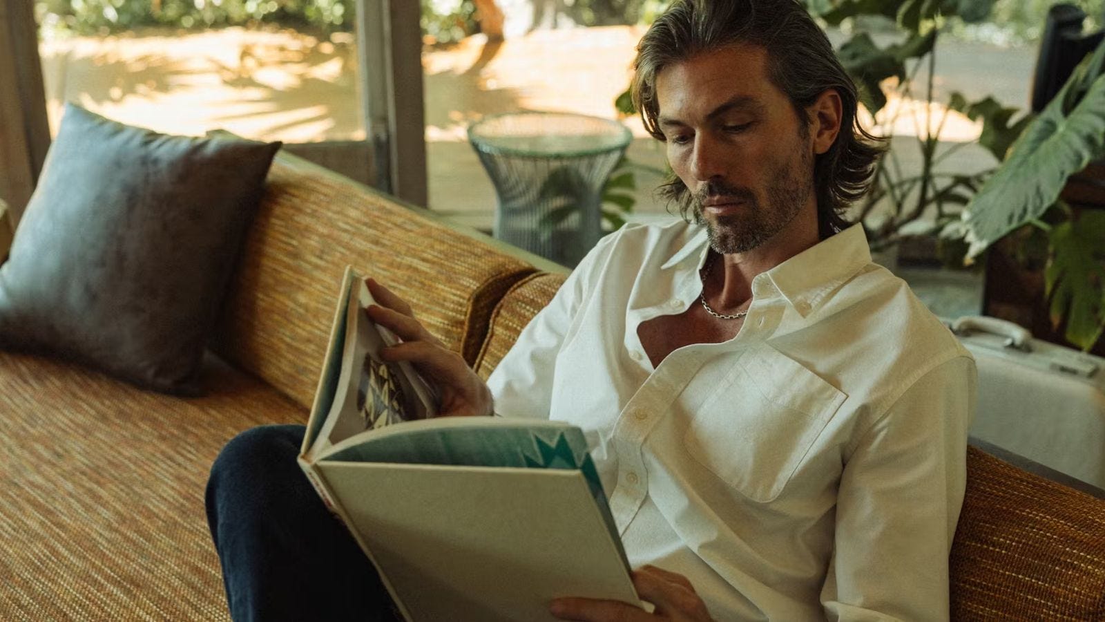 stylish man sitting on a couch reading a book