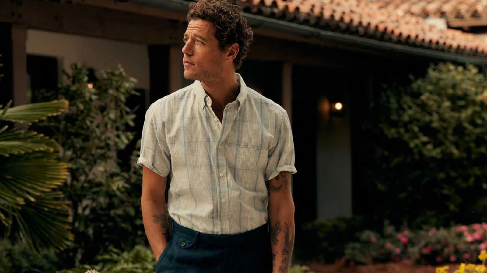 image of a man wearing a short-sleeve button-down shirt, gazing off and to the left, in front of a home with a Spanish-style roof