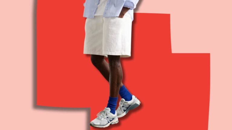 image of a man from the waist down, in a light blue shirt and off-white shorts, with New Balance sneakers and blue socks