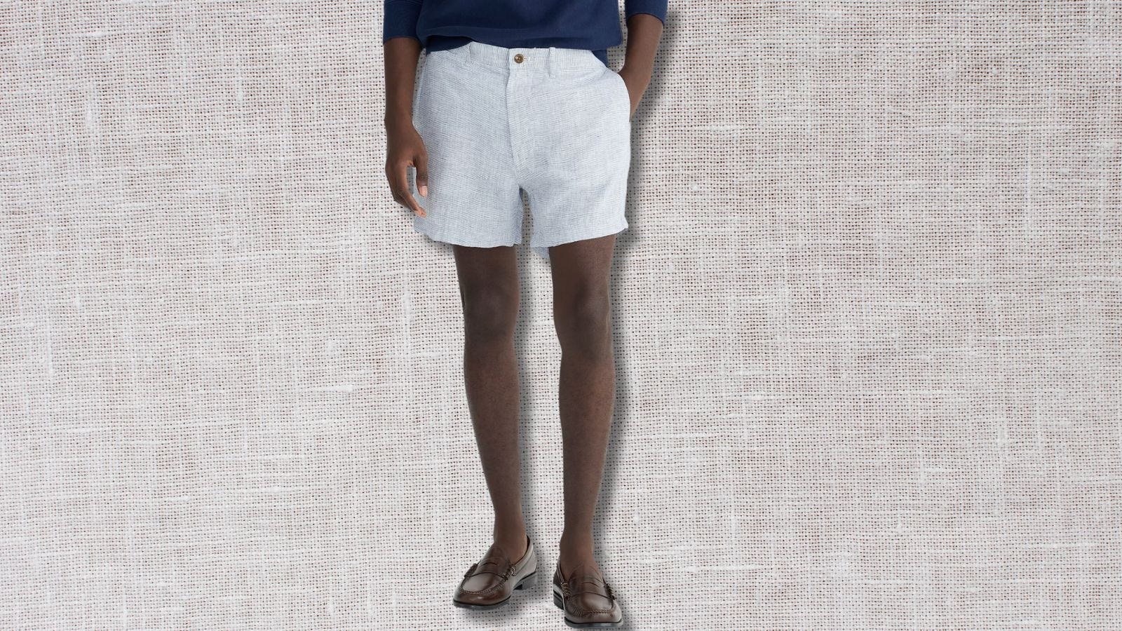 the lower half of a man wearing light bleu linen shorts against a tan linen background, men's linen shorts outfits 2024