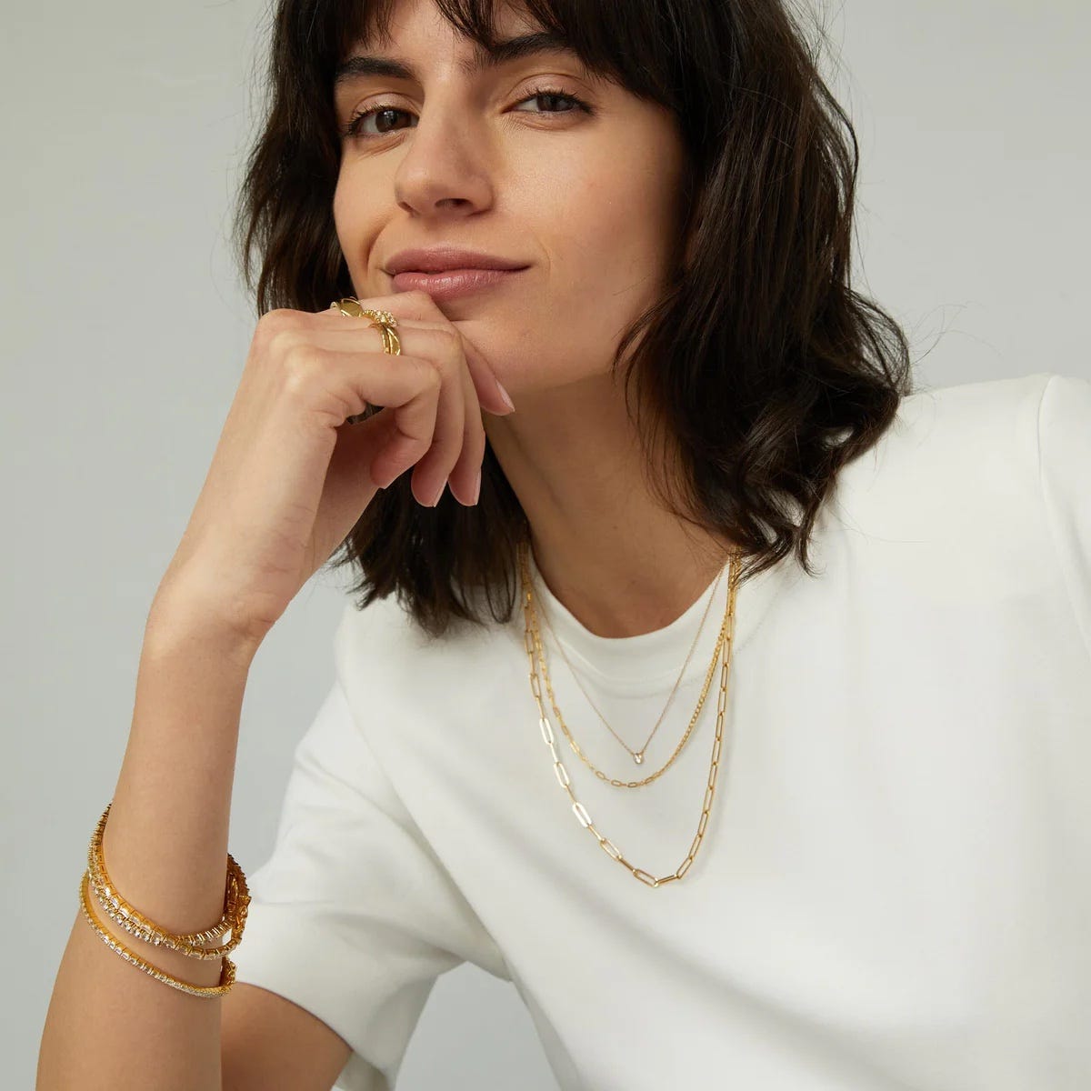 stylish woman wearing a white t-shirt with stacked gold necklaces around her neck and gold bracelets on her wrist