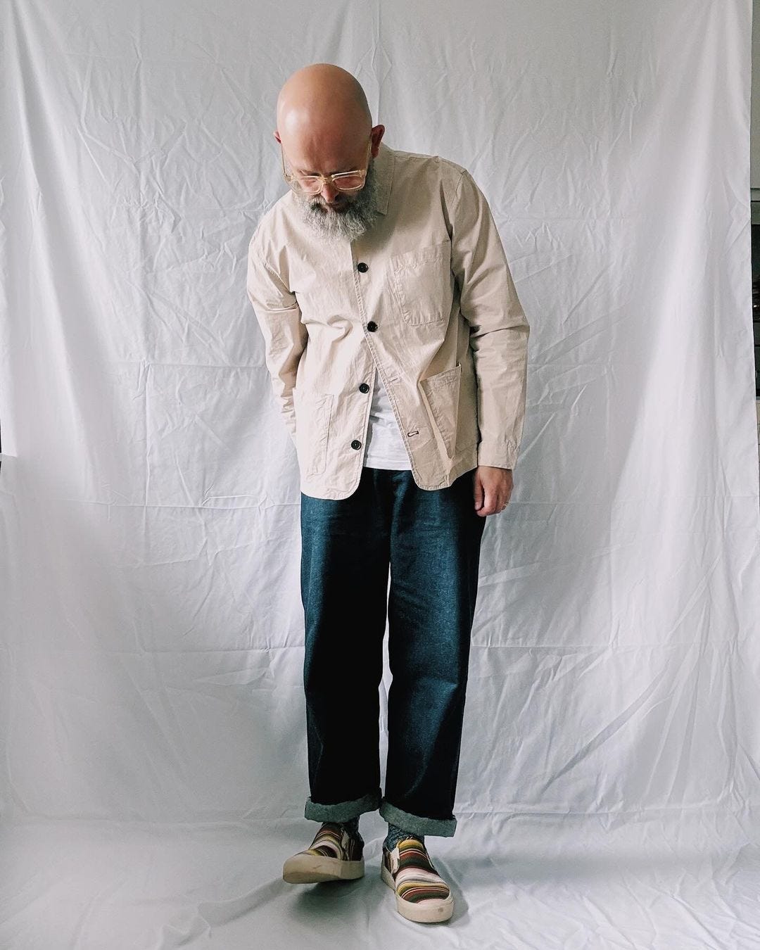 man wearing a bone-colored chore coat with dark jeans and sneakers