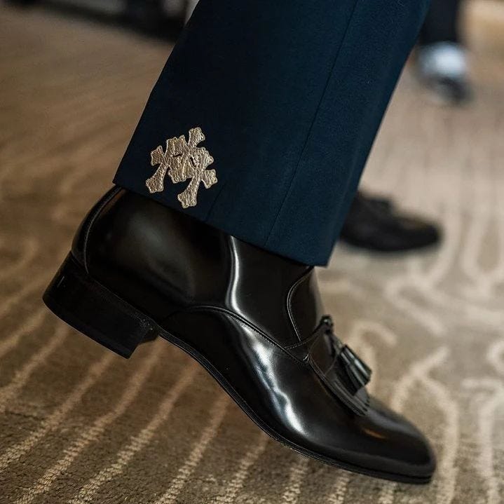 close-up of a man's leg in a navy suit with silver detailing at the hem, and black dress shoes