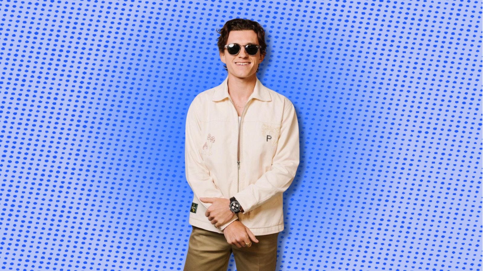 tom holland smiling in sunglasses wearing an off-white jacket and brown pants