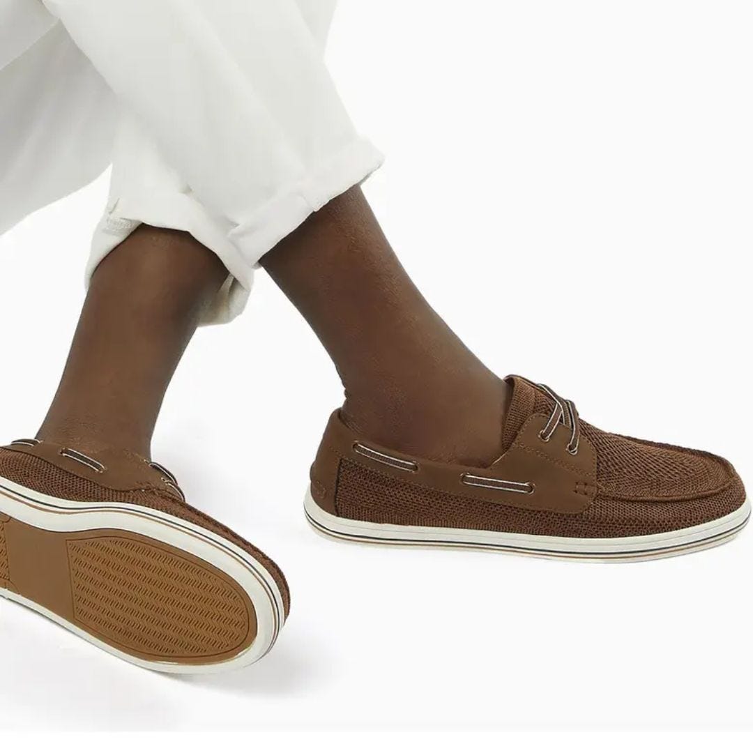 close-up of a man's legs wearing white pants rolled at the ankle and brown boat shoes in a knit material