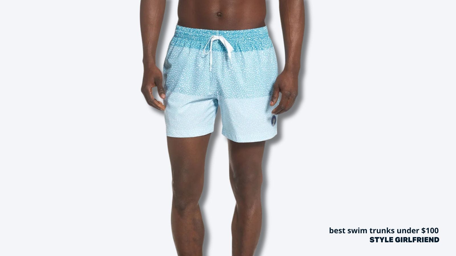close up of a man in light blue swim trunks against a grey background. text on-screen reads: best swim trunks under $100