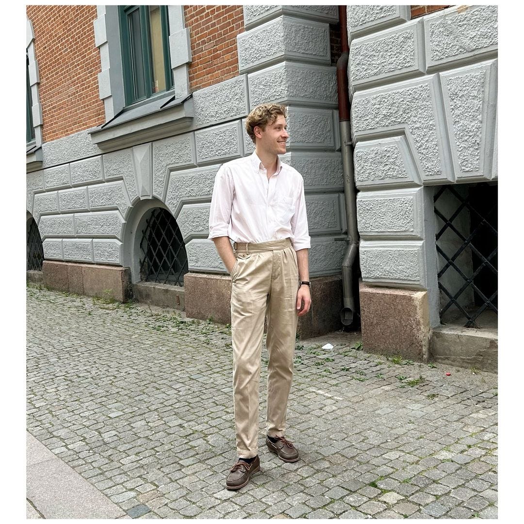 man in a white collared shirt, tan pants and boat shoes, standing outside on a cobblestone street