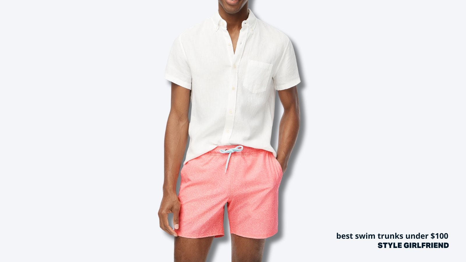 Close-up of man's torso and thighs. He wore a short-sleeved white shirt and salmon-colored drawstring swimming trunks.The text on the screen read: The Best Swim Trunks Under $100 | Style Girlfriend