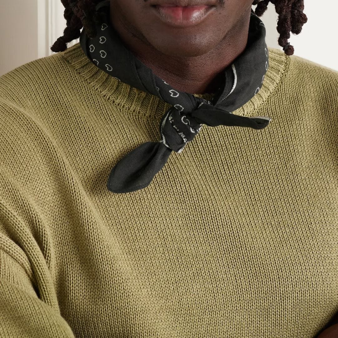 close-up of a man wearing an olive green sweater with a black patterned bandana