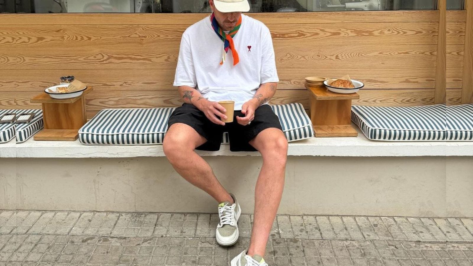 a man sitting outside a cafe in a white t-shirt, orange bandana, dark shorts, and light sneakers