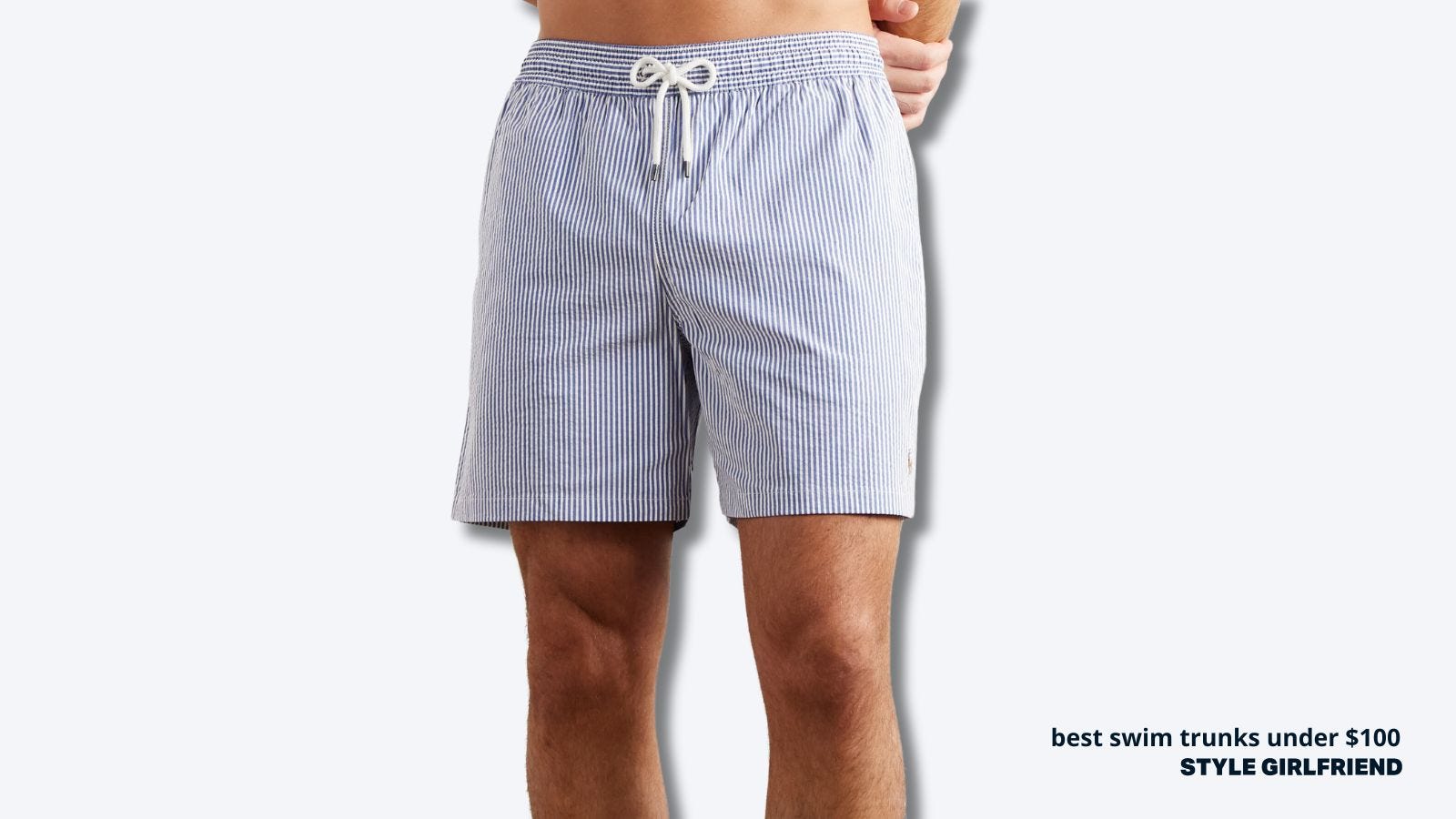 close up of a man wearing blue and white seersucker swim trunks with his hands behind his back. text on-screen reads: best swim trunks under $100, style girlfriend