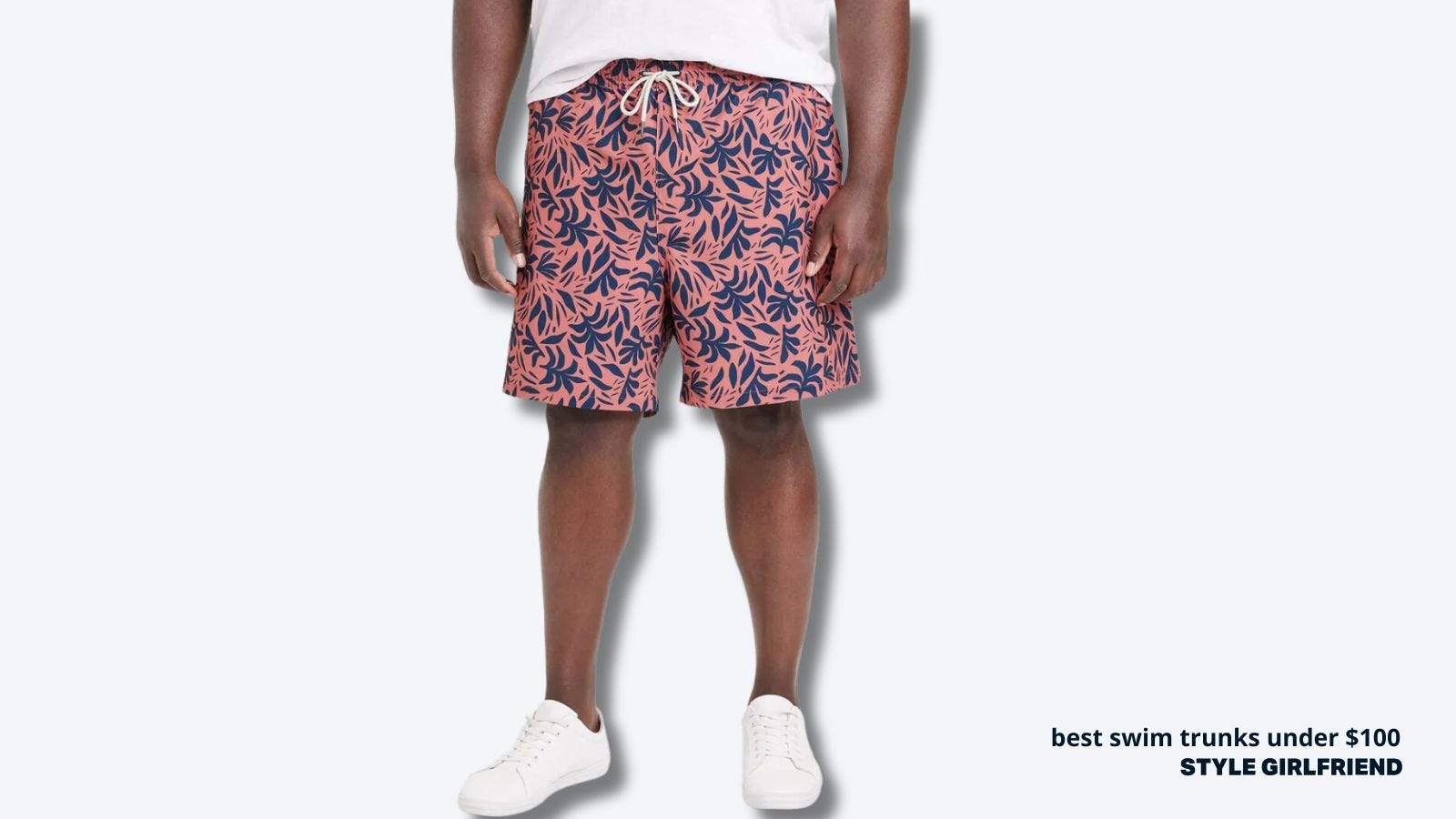 close-up of lower half of a larger man wearing a white t-shirt with pink and blue patterned swim trunks. text on-screen reads: best swim trunks under $100