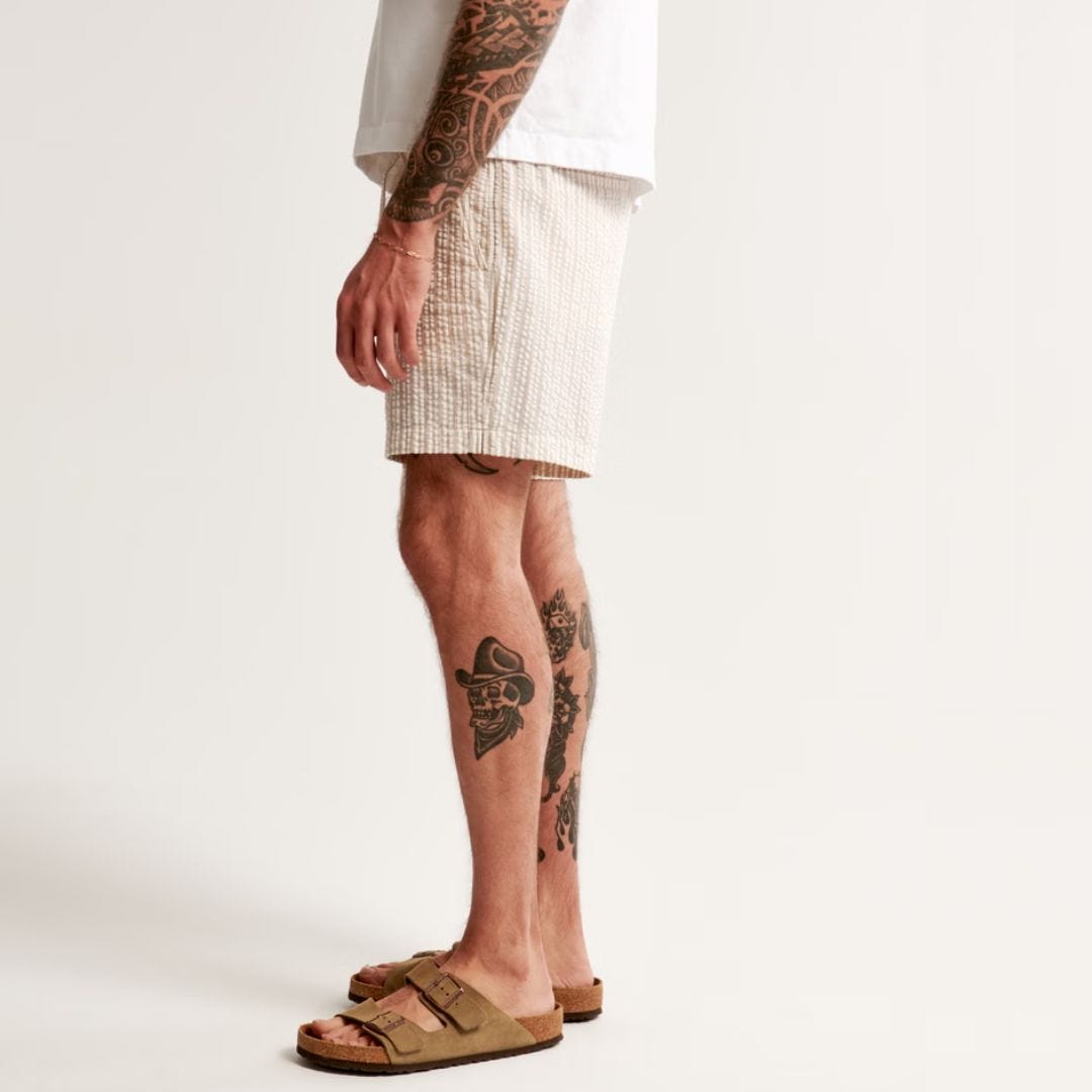 lower half of a man from the side wearing off-white shorts and sandals
