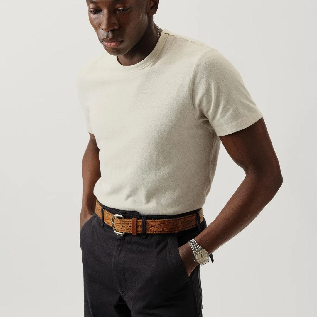 close-up of a man wearing an off-white t-shirt and dark pants with a brown belt