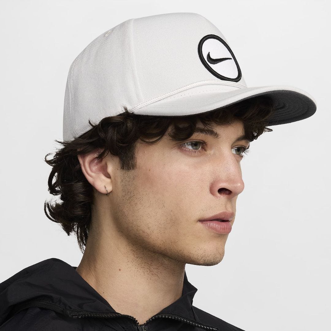 a close-up of a man wearing a white Nike baseball cap with the brand's swoosh logo on the front in black