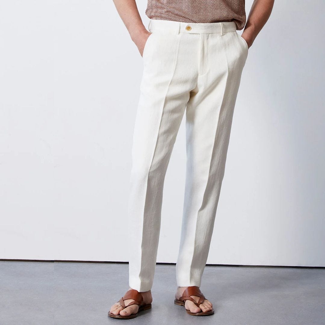 a man from the waist down wearing a pair of white dress pants and brown leather sandals, his hands are in his pockets, included in a roundup of light colored outfits for men