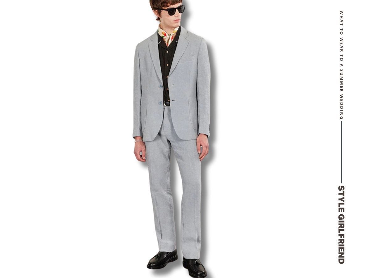 man in a tailored linen suit with a bandana tied around his neck and sunglasses. text on-screen reads: what to wear to a summer wedding