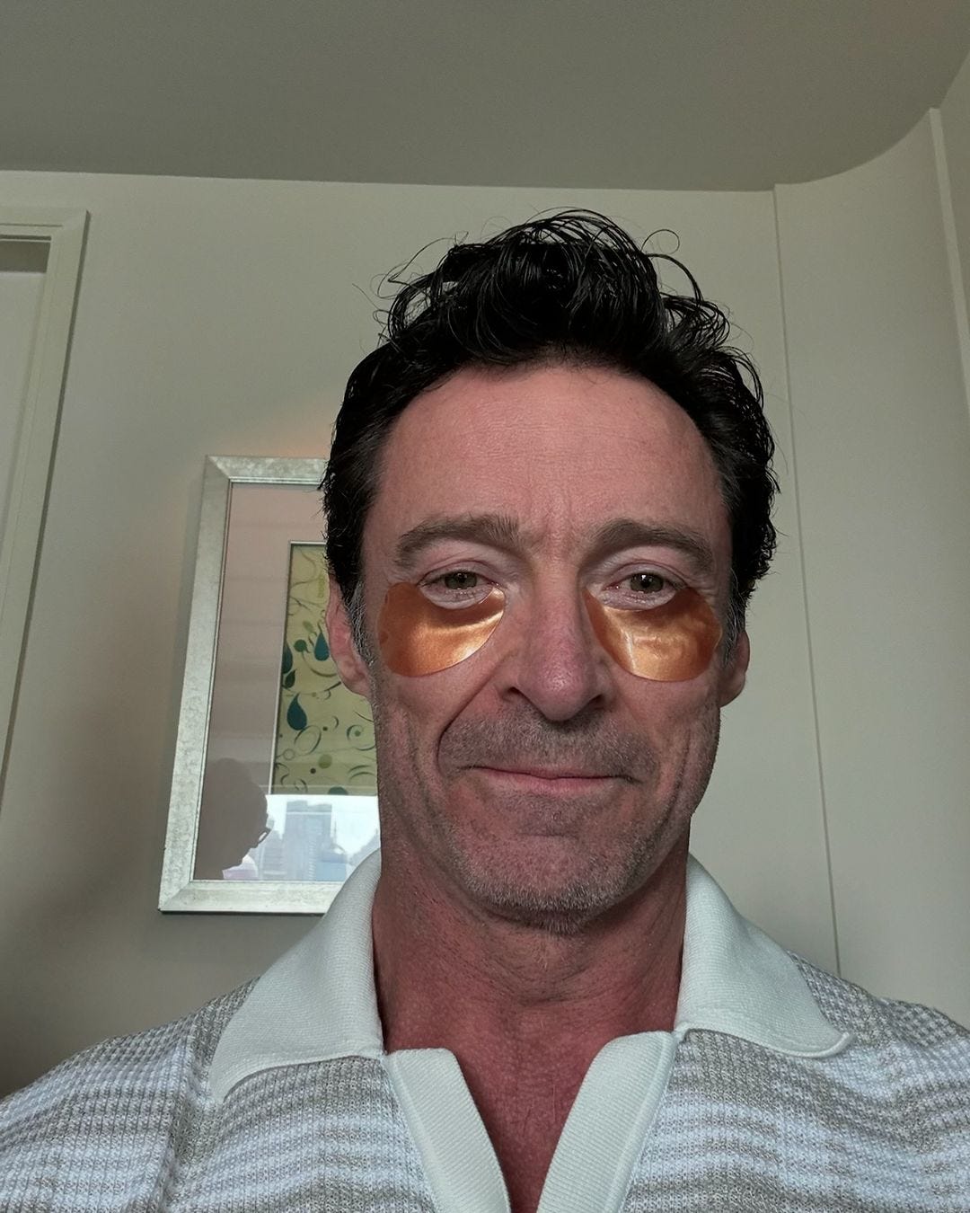 Actor Hugh Jackman smiles in a selfie wearing a gold iridescent eye patch under his eyes