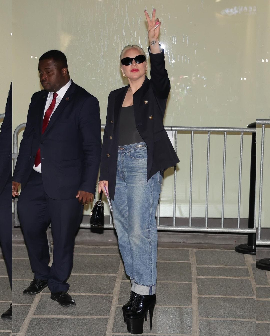 Lady Gaga in a navy blazer, black bodysuit, and jeans in Paris, flashing a peace sign