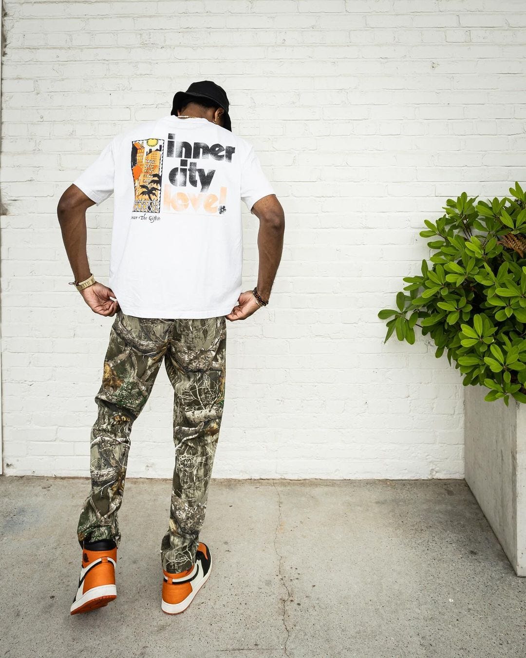 back of a man wearing a graphic t-shirt, camouflage pants, and orange nike sneakers