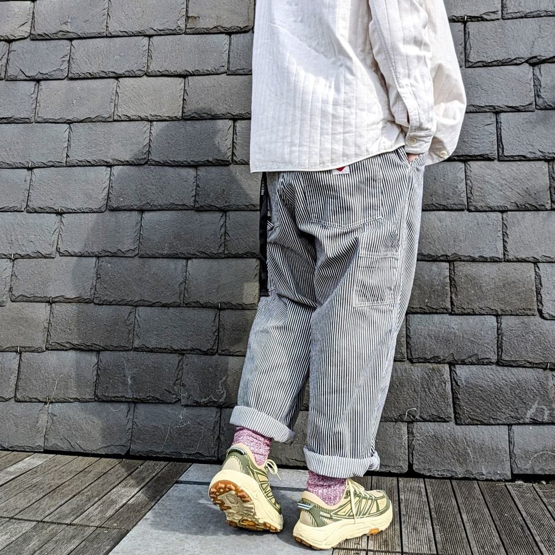 lower half of a man from behind, wearing striped carpenter pants rolled at the ankles with sneakers and tall socks