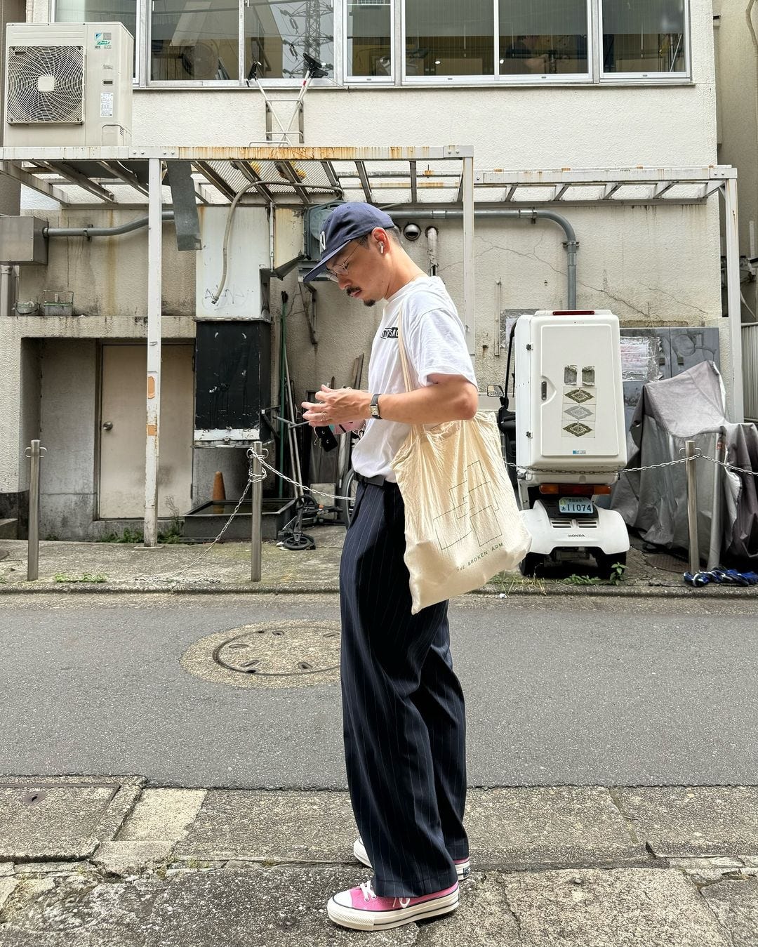 man from the side, standing in an alley wearing a blue baseball cap, white t-shirt, navy pants and pink sneakers