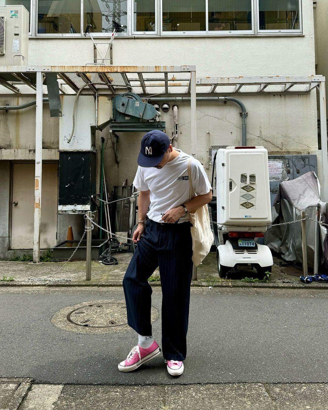 man standing in an alley wearing a blue baseball cap, white t-shirt, navy pants and pink sneakers