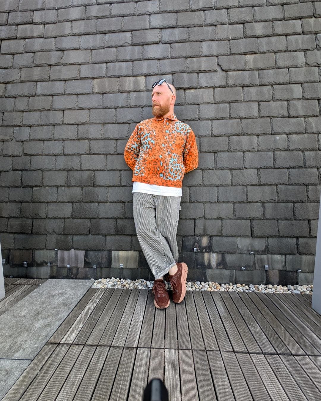 man standing against a stone wall in an orange animal print shirt with train conductor stripe pants