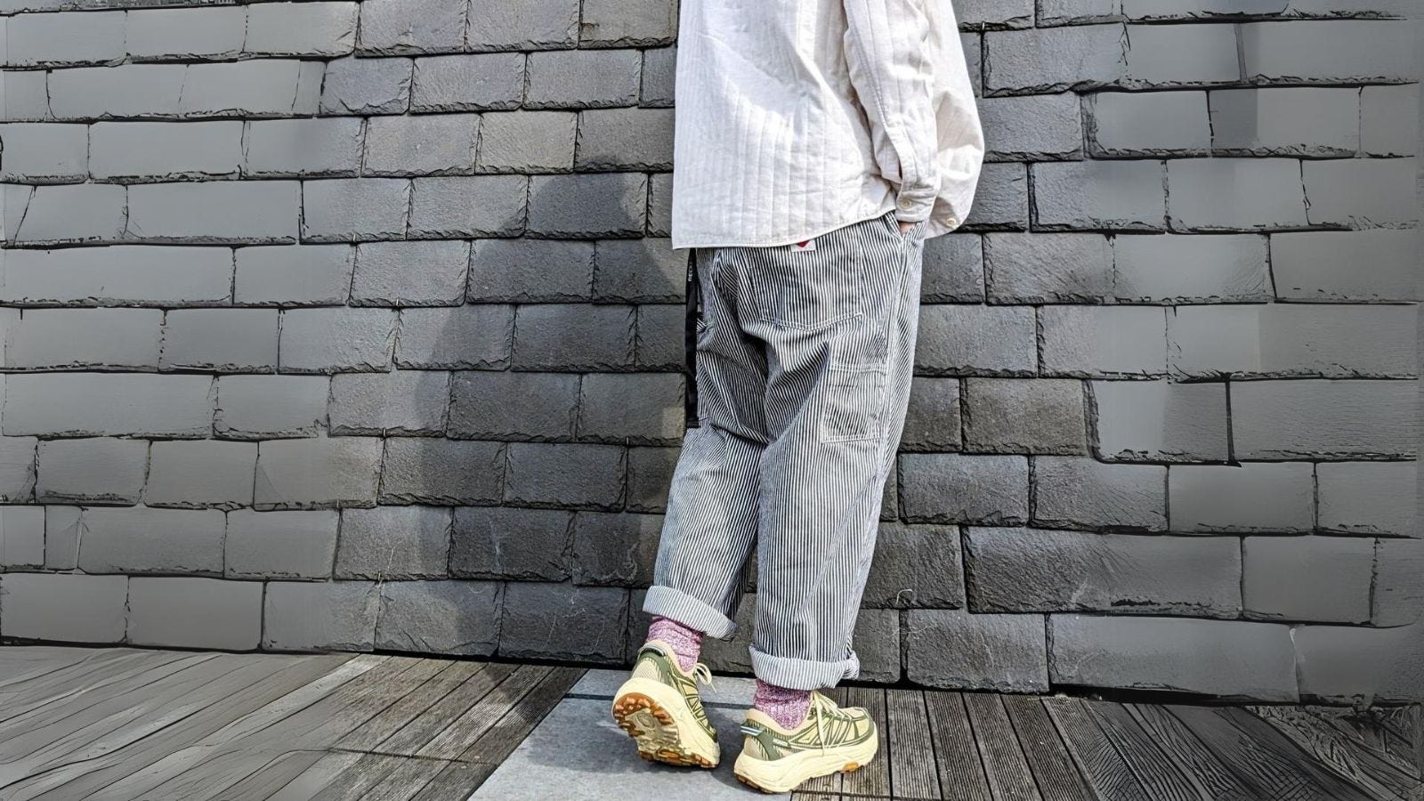 man in train conductor stripe pants, standing against a brick wall