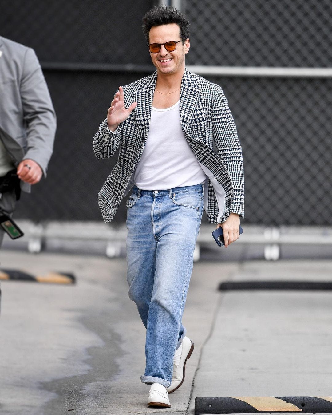 actor Andrew Scott wearing a blazer and jeans, waving at the camera