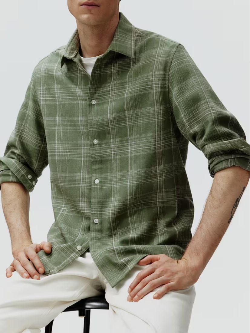 Close-up from the waist up of a man wearing a green flannel shirt sitting on a stool