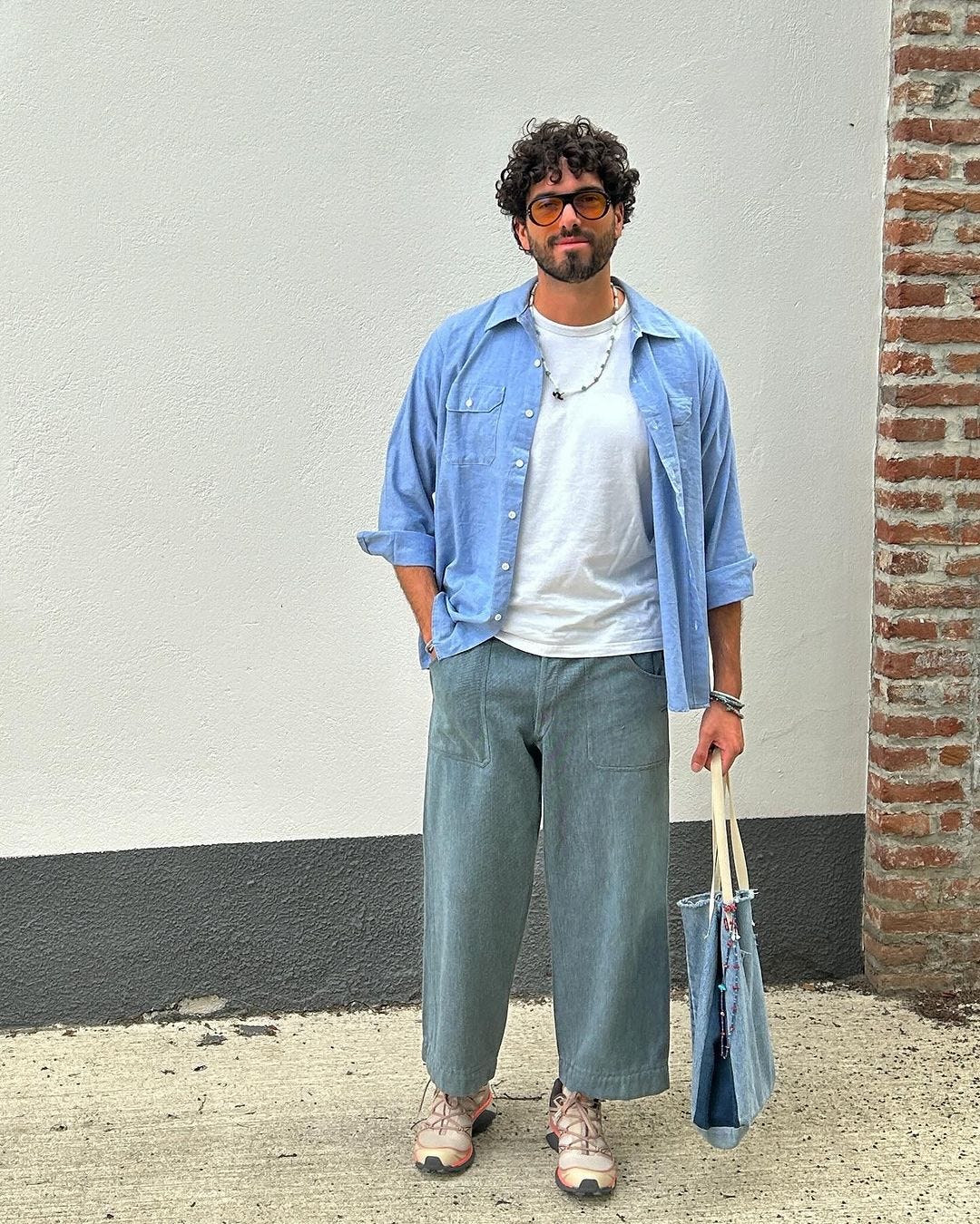 man wearing a chambray shirt open over a white t-shirt with wide legged jeans and sneakers