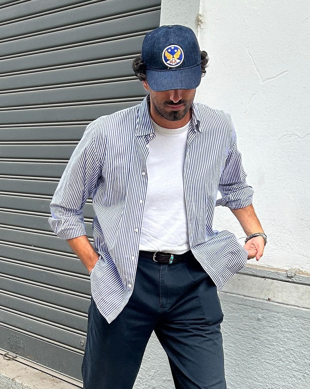 Close-up of a man wearing a striped shirt, white T-shirt, dark blue pants and a blue baseball cap