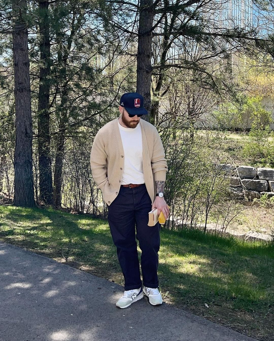 man standing outside in an oatmeal-colored cardigan over a white shirt with dark pants and sneakers