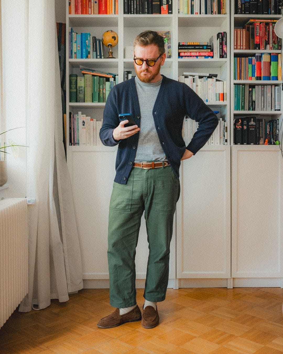 man wearing a navy v-neck cardigan over a grey t-shirt with green pants and a brown belt