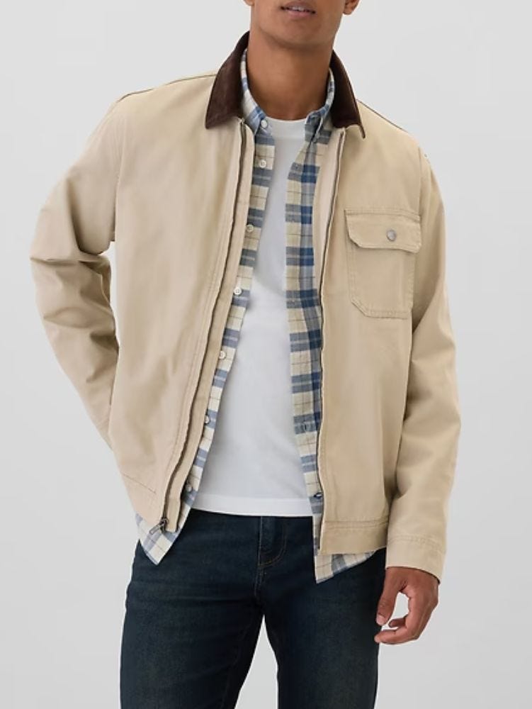 man from the neck down wearing a tan canvas work jacket over a plaid shirt and white t-shirt with dark pants