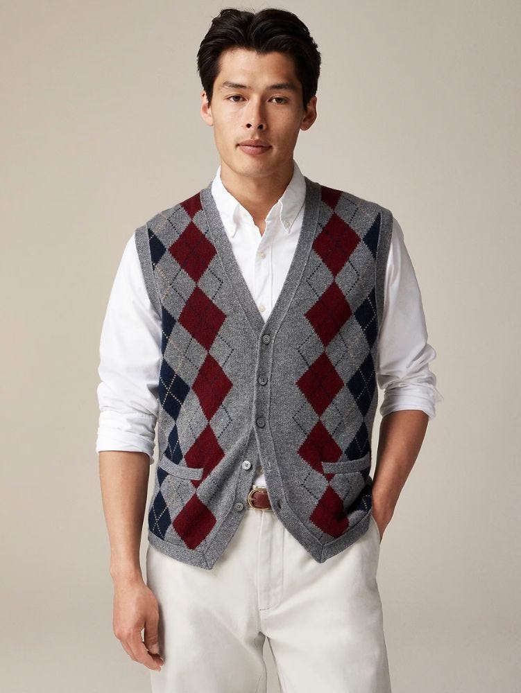 Man wearing gray argyle sweater vest, white buttoned shirt and casual pants from waist up