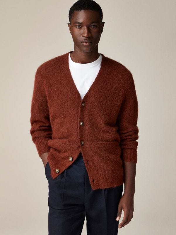 close-up of a man wearing a brown v-neck cardigan over a white crewneck t-shirt