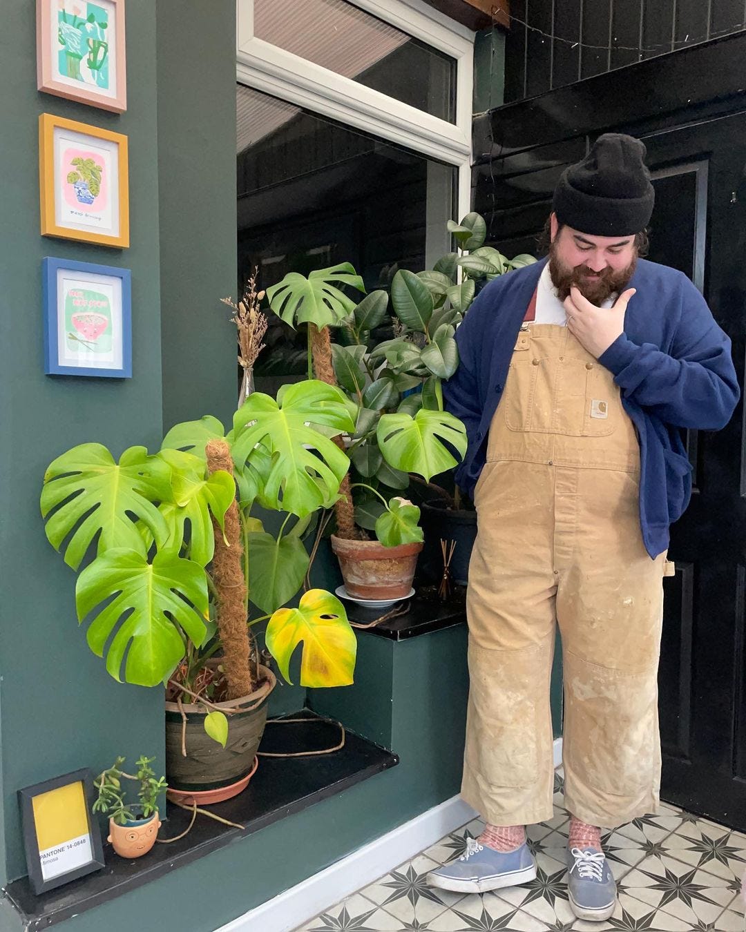 man wearing Carhartt overalls with a navy cardigan and blue sneakers