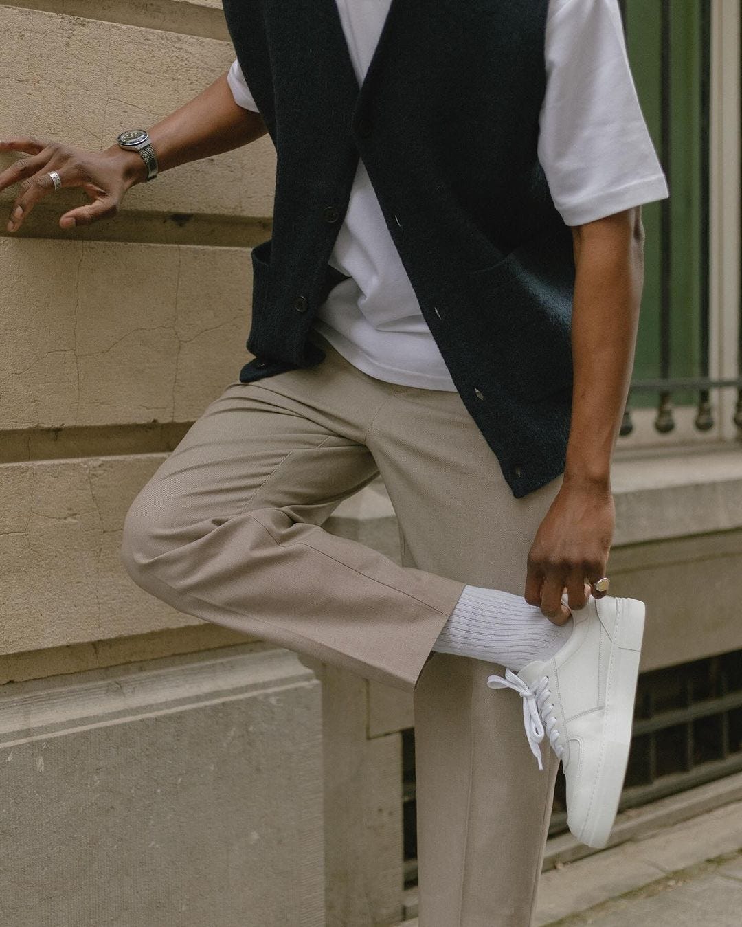 close-up of a man wearing a white t-shirt, dark vest, tan chinos, white socks, and white sneakers