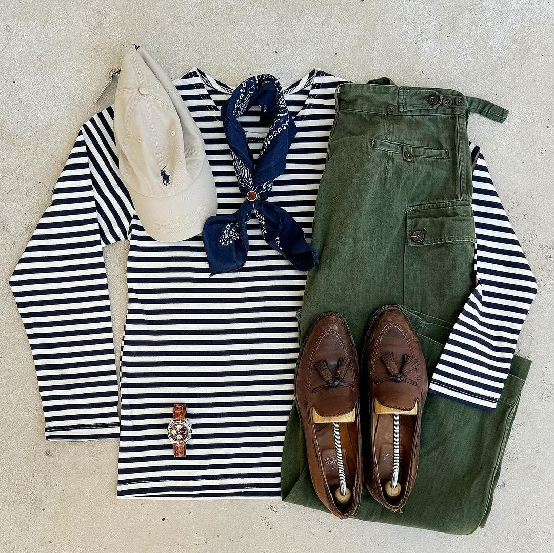 Flat lay of casual men's clothing including blue and white striped long sleeve shirt, blue bandana, off-white baseball cap, green pants and brown tassel loafers