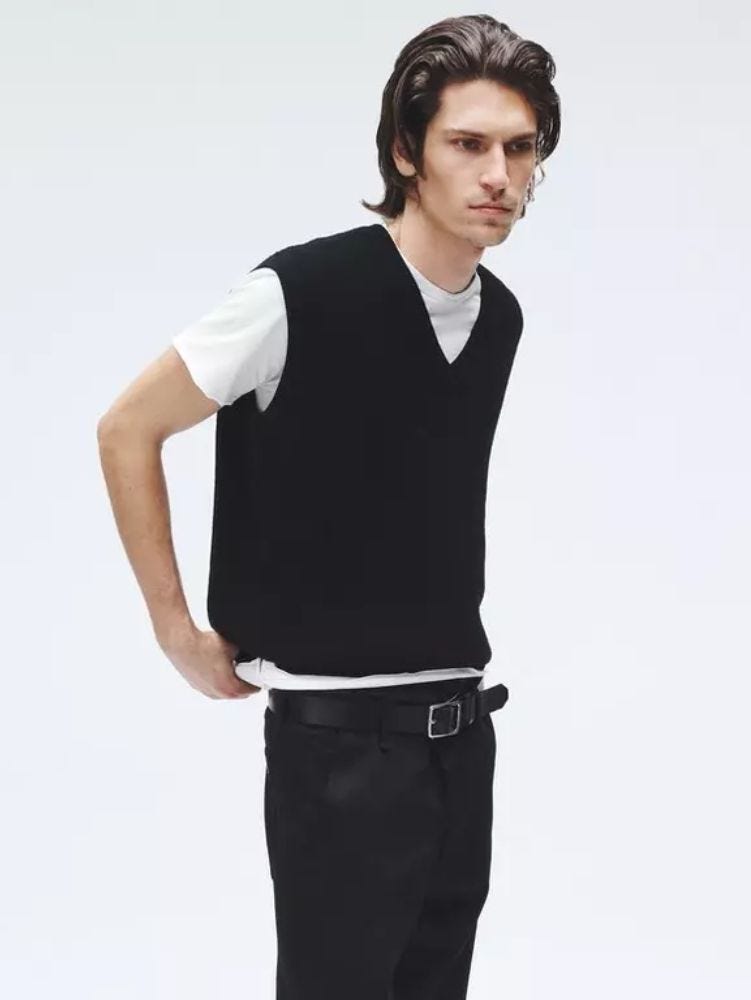 Man wearing black V-neck sweater vest, white T-shirt, black pants and black belt from waist up