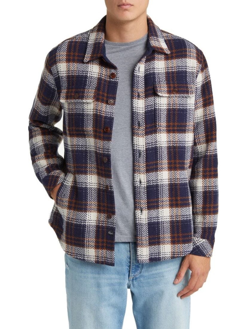 Close-up of a man wearing a burgundy and navy plaid flannel shirt, gray T-shirt and light blue jeans