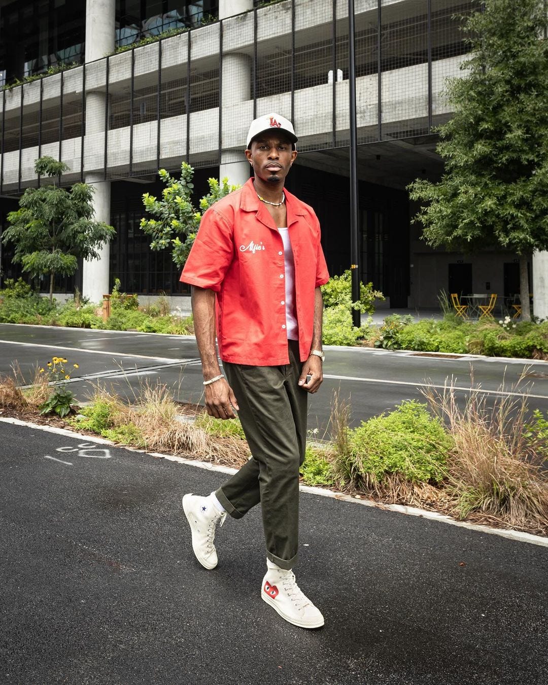 Man walking down the street wearing red short-sleeved shirt, white vest, olive green pants and high-top Nike sneakers