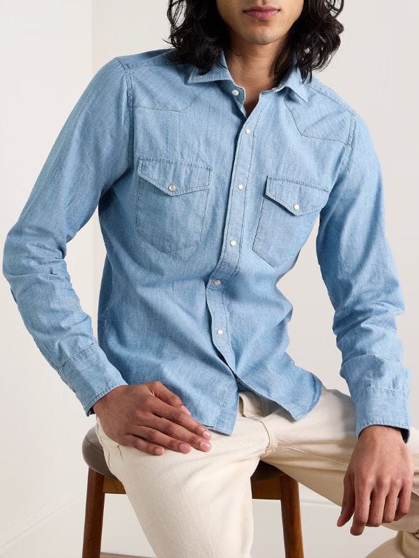 man from the waist up, sitting on a stool and wearing a buttoned chambray shirt