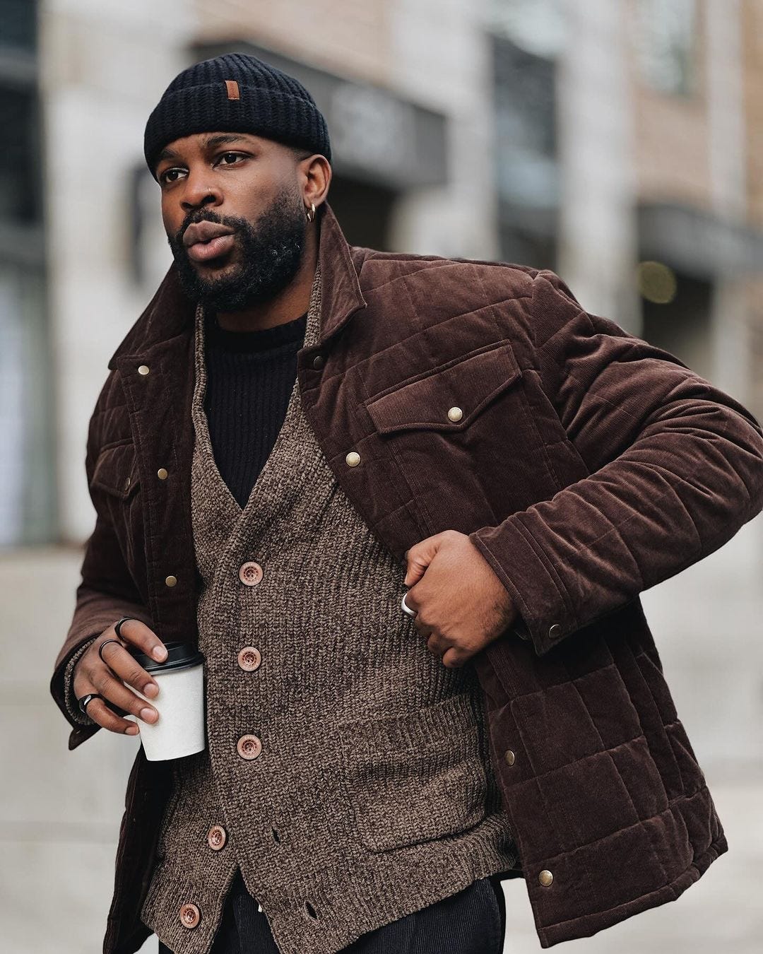 man wearing a chocolate-brown puffer jacket over a marled brown cardigan and black shirt