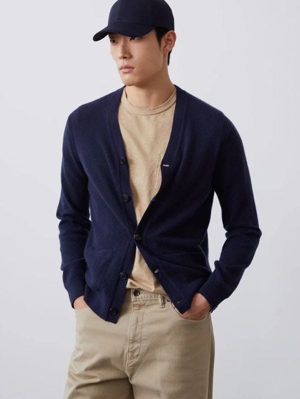 man from the waist up wearing a navy v-neck cardigan over a tan t-shirt with tan-colored twill pants