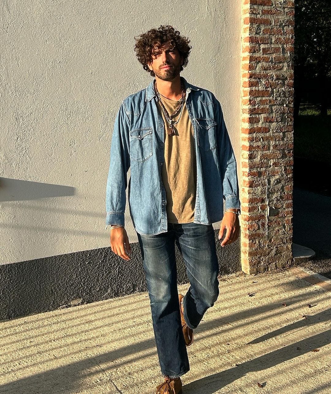 man standing outside wearing a denim shirt over a tan t-shirt with dark jeans