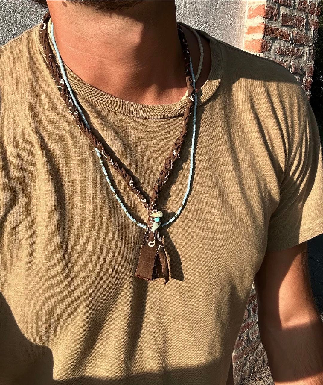 close up of a man wearing a tan t-shirt with two necklaces